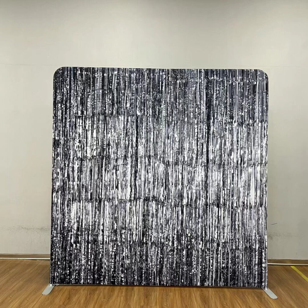 A shimmering black sequin event backdrop standing on a wooden floor; contact us to book this glamorous photo background for your next party.