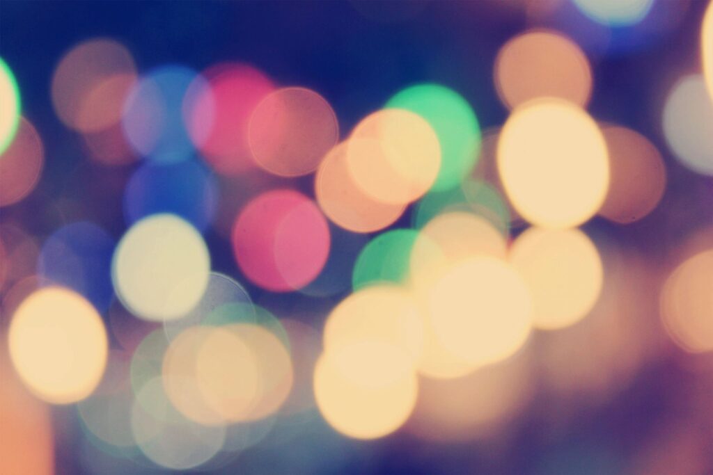 Colorful out-of-focus bokeh lights in shades of yellow, blue, and pink creating a festive party atmosphere; contact us to book your vibrant night tour with Trill On Wheels.